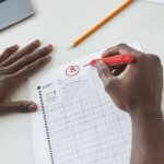 рука вычеркивает лишние события из длинного списка ставок красной ручкой